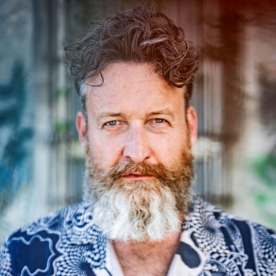 Sven kijkt serieus de camera in. Hij draagt een blauw met witte blouse en de achtergrond is vervaagd.