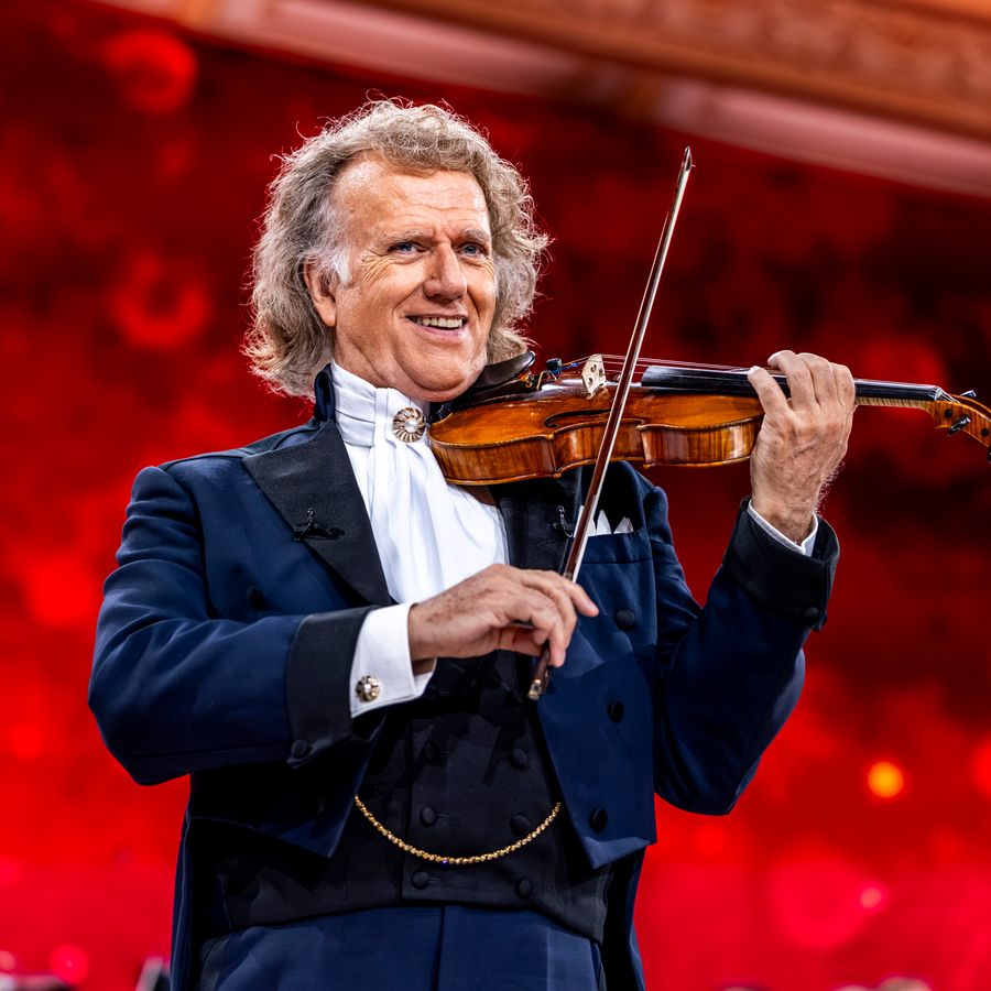 André Rieu staat in een blauwpak en heeft zijn viool onder de kin. 