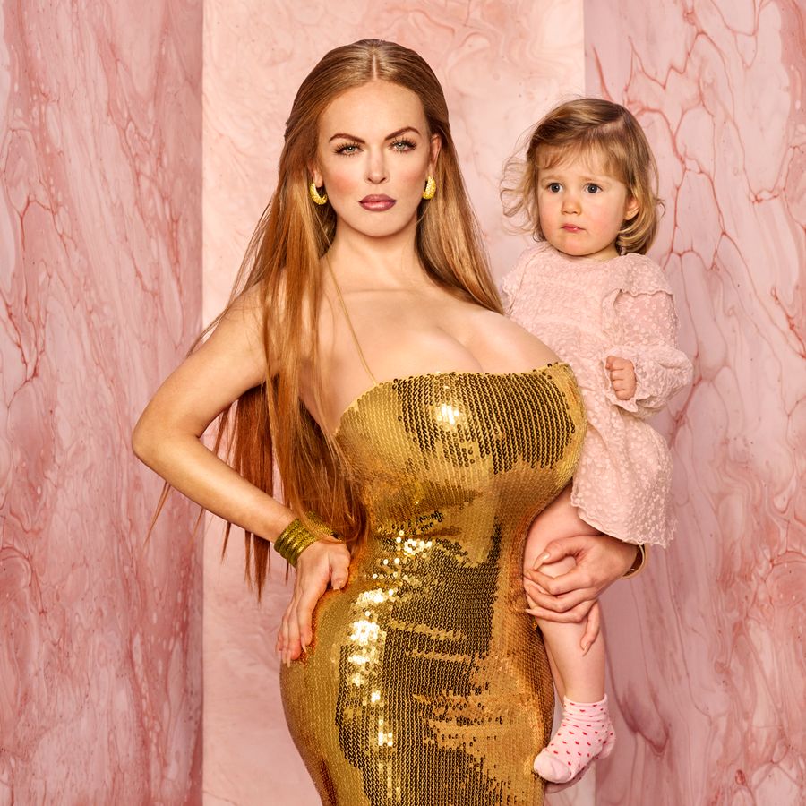 Een vrouw in een gouden glitterjurk. Ze houdt een klein meisje vast op haar heup. De achtergrond is roze.