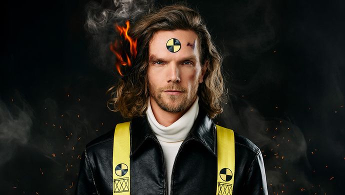 Ruud kijkt strak naar voren de camera in. Op zijn voorhoofd staat een cirkel met geel en zwart. Zijn haar staat aan de linkerkant in brand. Achter hem is het zwart en komen er vuurvonken tevoorschijn en hij heeft een zwart jasje aan met gele banden om zijn schouders met hetzelfde tekentje als op zijn voorhoofd erop.