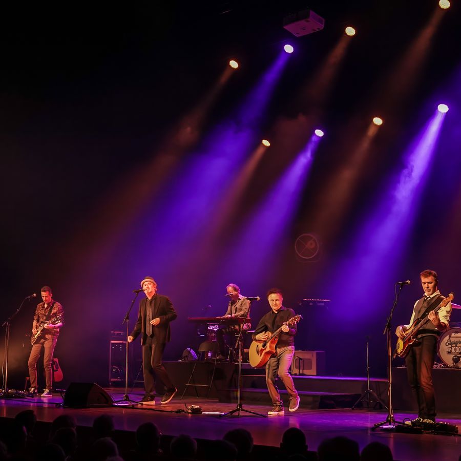 Een band staat te spelen op een podium met paarse en rode lampen.