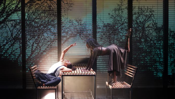 2 mensen buigen over een tafel heen en staan op een bankje naast de tafel.