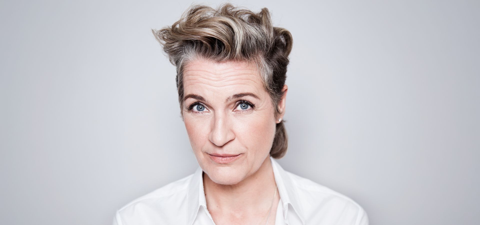 Margriet staat voor een grijze achtergrond en kijkt met een blik van twijfel naar de camera. Haar wenkbrauwen staan omhoog.