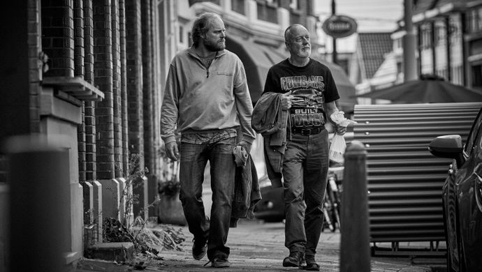 Zwart wit foto met daarop twee mannen lopend over straat. 