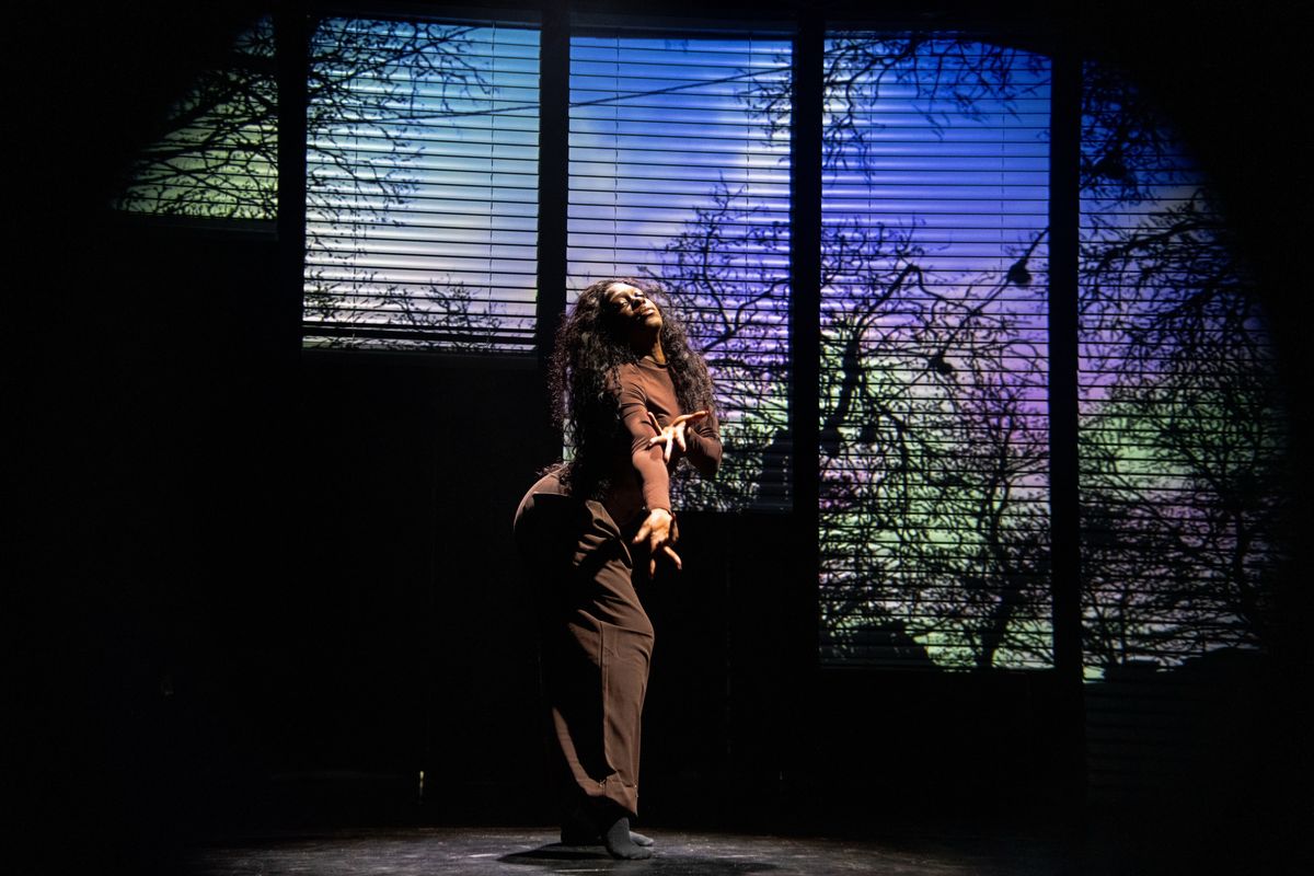 Een vrouw staat te dansen met één hand naar voren. Ze heeft een verdrietige uitdrukking en heeft haar ogen gesloten.