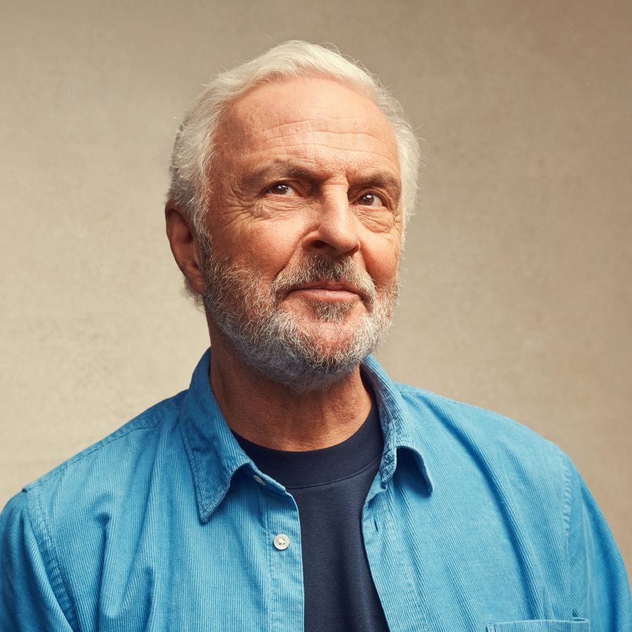 Een man kijkt schuin omhoog en heeft een glimlach. De achtergrond is bruin. 