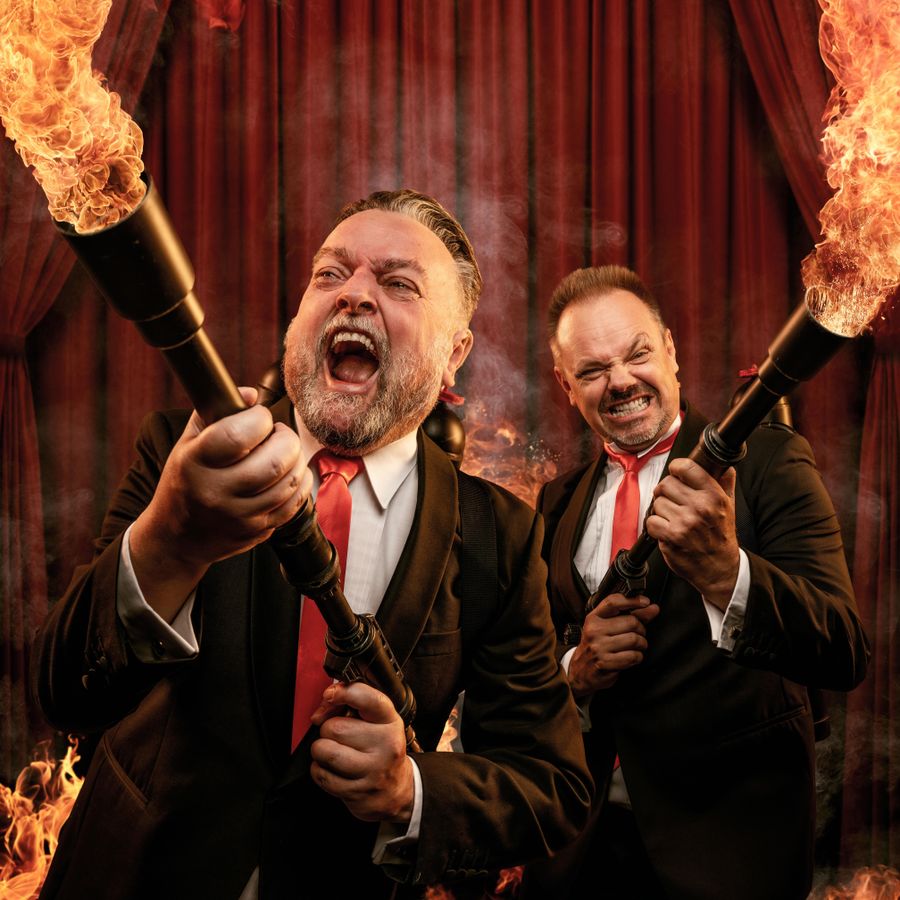 Arie en Silvester staan allebei in pak. Ze kijken boos naar voren en hebben een geweer in hun handen waar vuur uitkomt. Op de achtergrond is er een rood theaterdoek te zien.