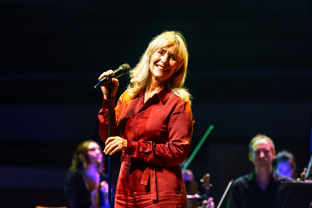 Angela staat op het podium achter een microfoon en glimlacht.