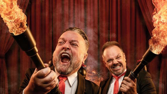 Arie en Silvester staan allebei in pak. Ze kijken boos naar voren en hebben een geweer in hun handen waar vuur uitkomt. Op de achtergrond is er een rood theaterdoek te zien.