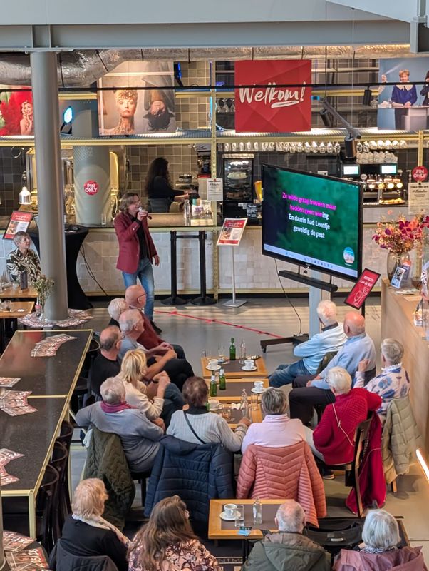 Een groep mensen zitten voor een scherm waar de songtekst op te zien is. 