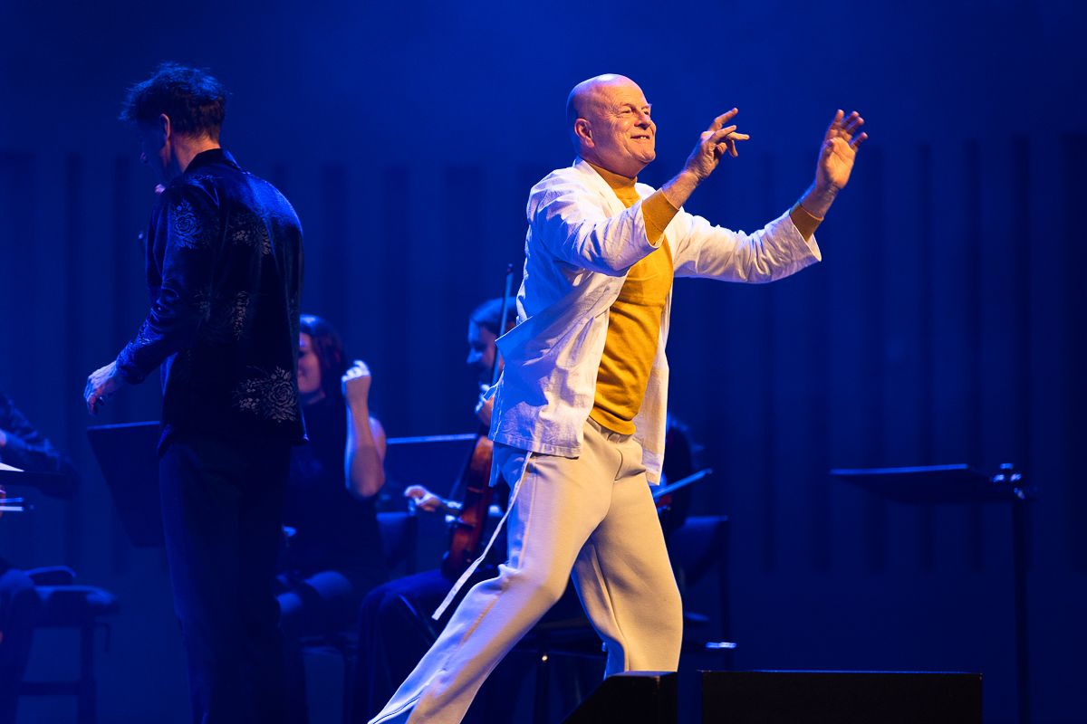 Andrew staat op het podium met zijn handen te bewegen en kijkt lachend het publiek in.