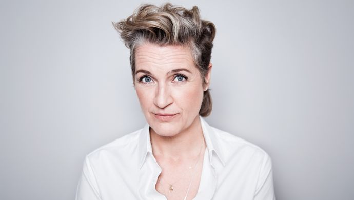 Margriet staat voor een grijze achtergrond en kijkt met een blik van twijfel naar de camera. Haar wenkbrauwen staan omhoog.