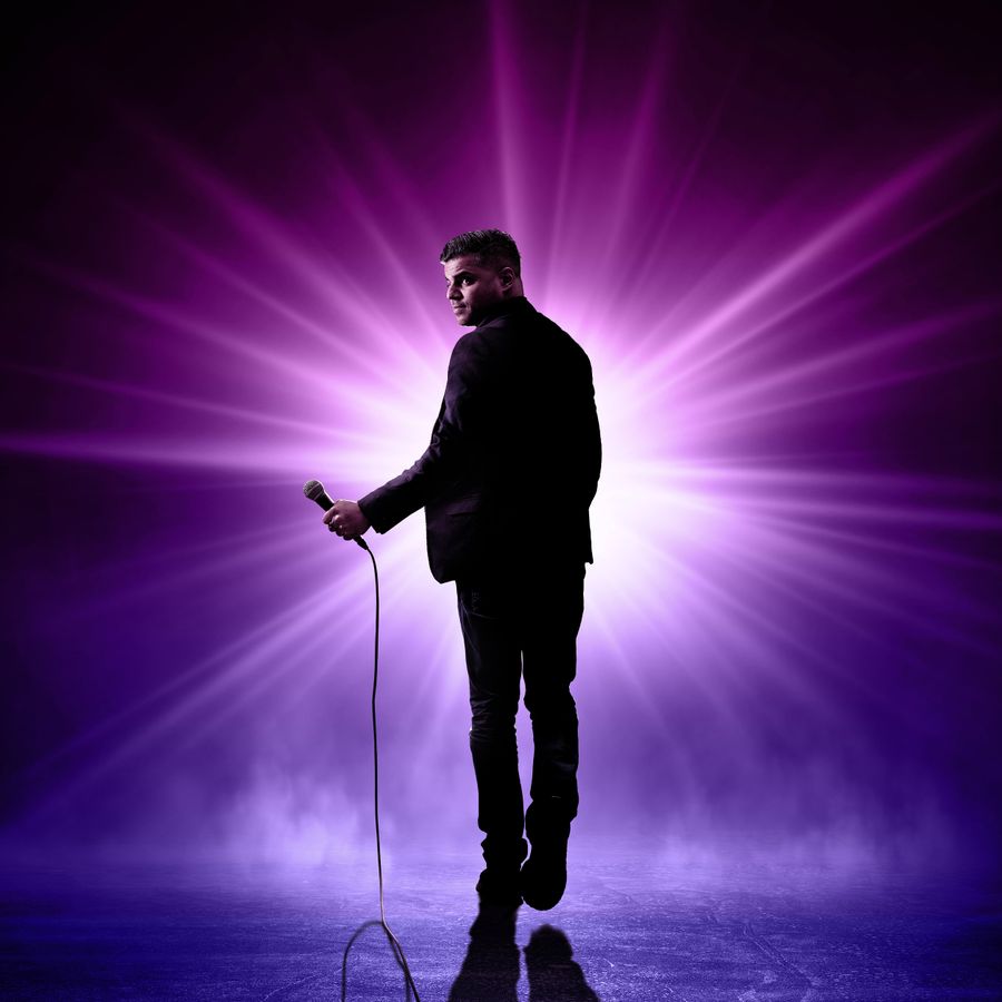 silhouette van en man met microfoon tegen een paarszwarte achtergrond met felle spotlight. 
