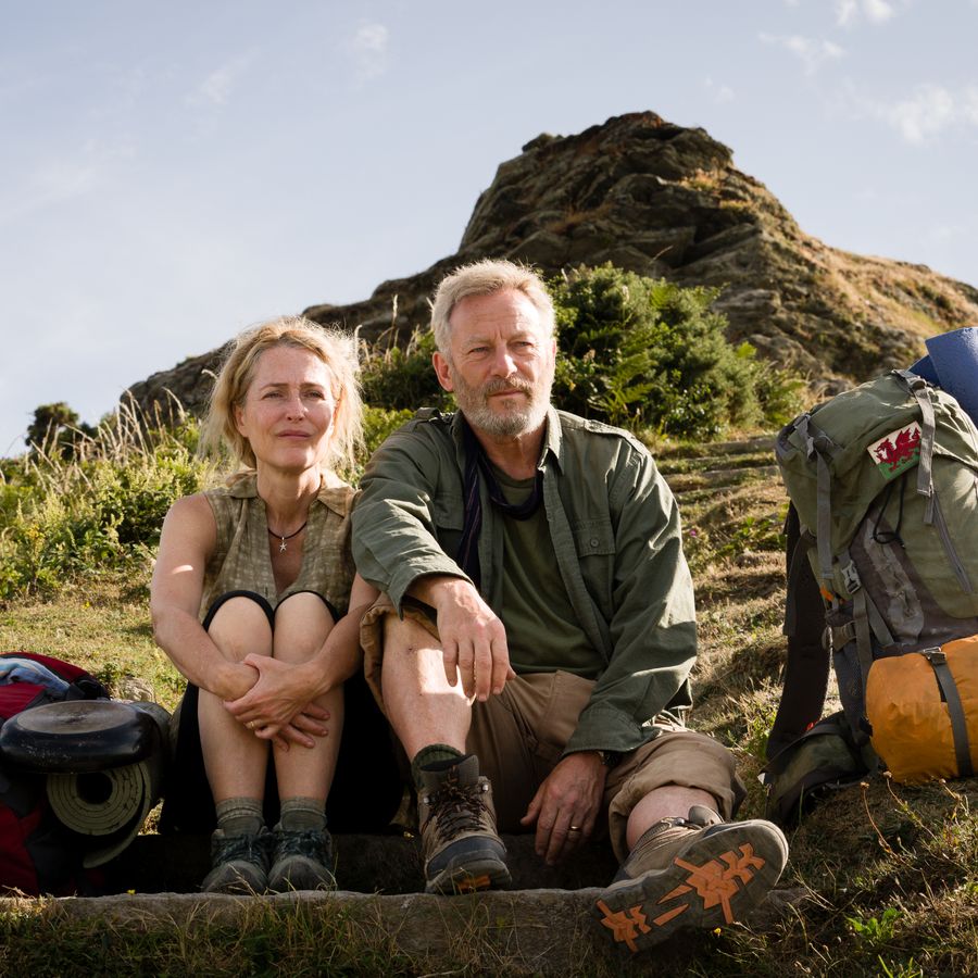 Een man en een vrouw zitten op de grond op een berg, met hun rugzakken naast hen, en kijken met een ernstige blik voor zich uit.