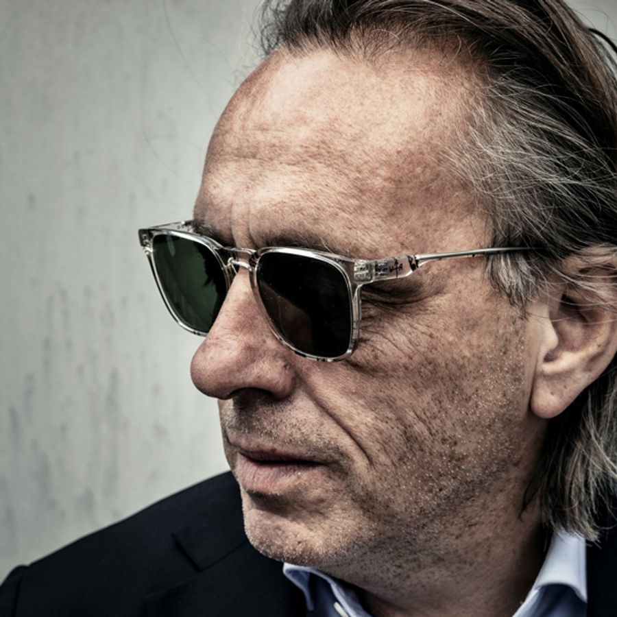 Man, Marcel van Roosmalen zelf, met half lang achterover gekamd haar en zonnebril kijkt opzij. 