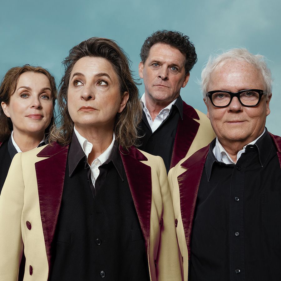 2 mannen en 2 vrouwen alle vier in zelfde kleurstelling gekleed met bruine trui en beige regenjas vooruit kijkend. 