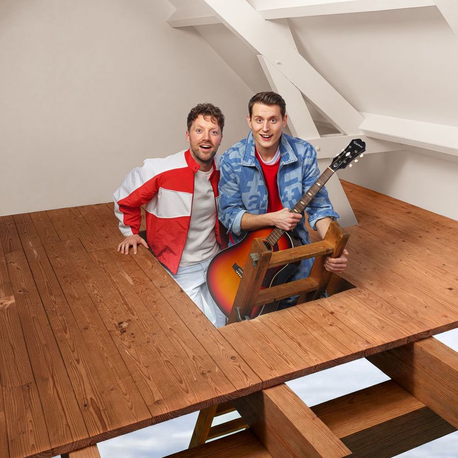 Twee mannen komen verrast op een zolderkamer. Ze staan allebei op een trapje dat uit een houten vloer komt en een van die mannen heeft een gitaar vast.