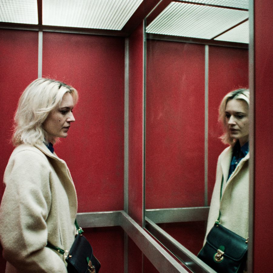 Vrouw met blond haar staart in een spiegel in een lift. 