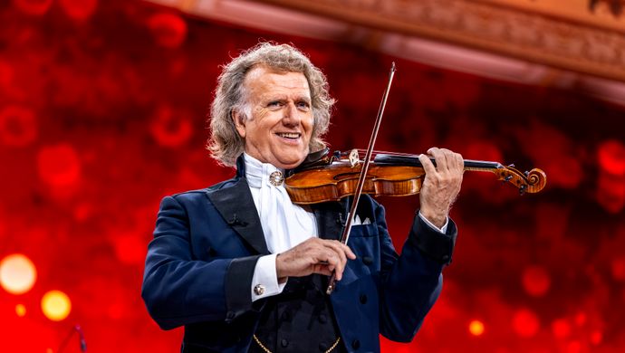 André Rieu staat in een blauwpak en heeft zijn viool onder de kin. 
