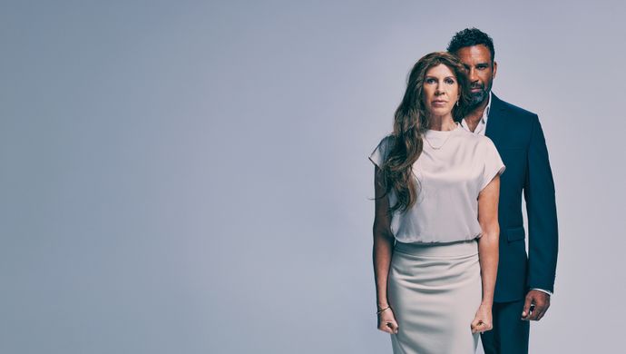 Een vrouw staart vooruit terwijl er een man half achter haar staat met een boze blik. 