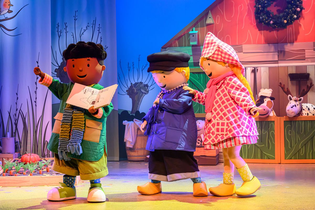 Fien en Teun lopen over een decor van een boerderij achter een pop aan met een boek in zijn handen.