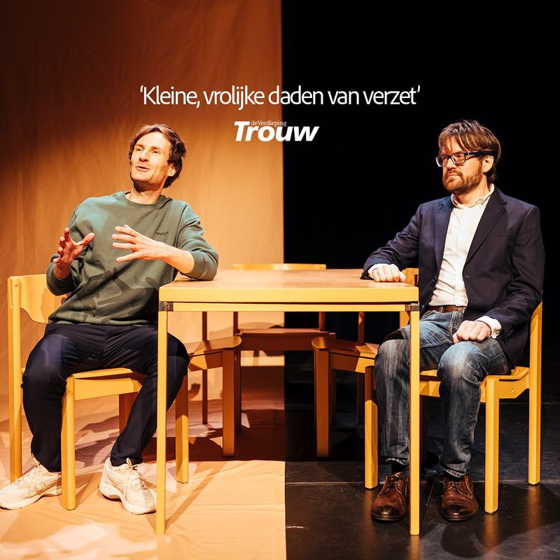 Twee mannen zitten aan een tafel op een podium. Een man vertelt en maakt handgebaren terwijl de ander serieus kijkt en luisterd. Boven heen staat een persquote: kleine, vrolijke daden van verzet van de Trouw.