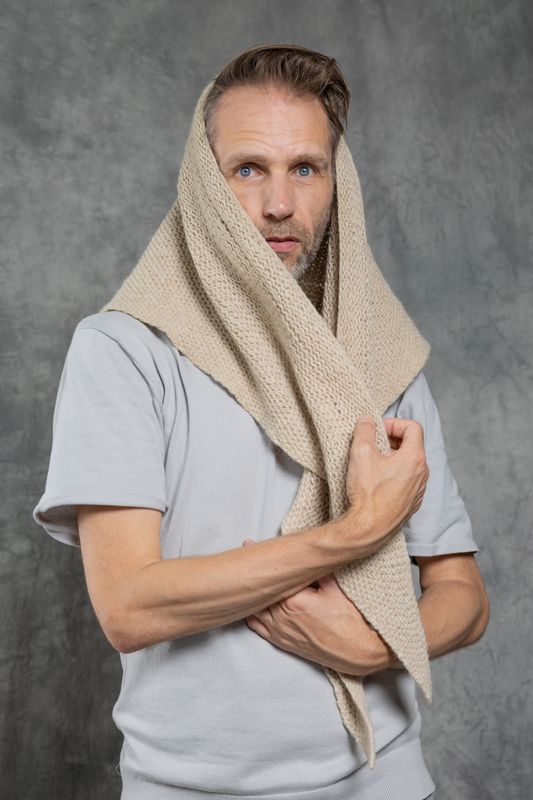 Een man kijkt angstig naar de camera en heeft een doek half over zijn hoofd. Hij houd het doek voor zijn borst vast. Hij staat voor een grijze achtergrond.