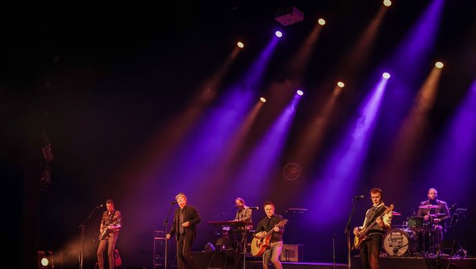 Een band staat te spelen op een podium met paarse en rode lampen.