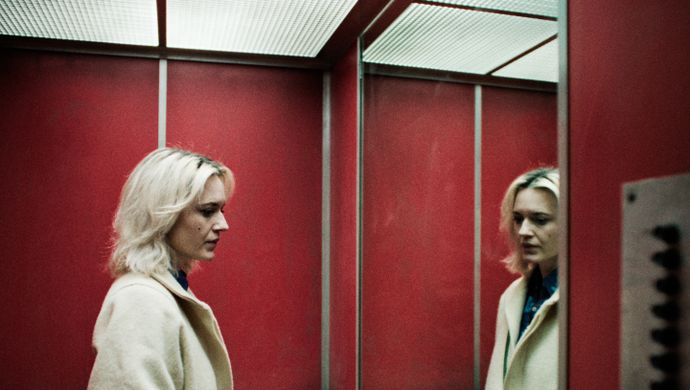 Vrouw met blond haar staart in een spiegel in een lift. 