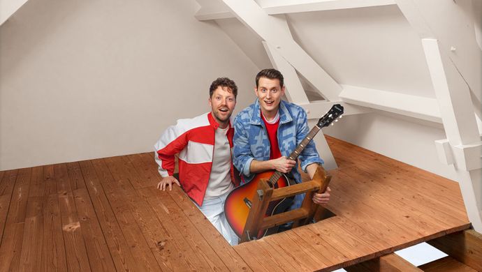 Twee mannen komen verrast op een zolderkamer. Ze staan allebei op een trapje dat uit een houten vloer komt en een van die mannen heeft een gitaar vast.
