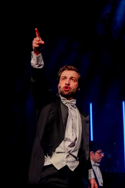 Een man in pak wijst naar boven en zingt.