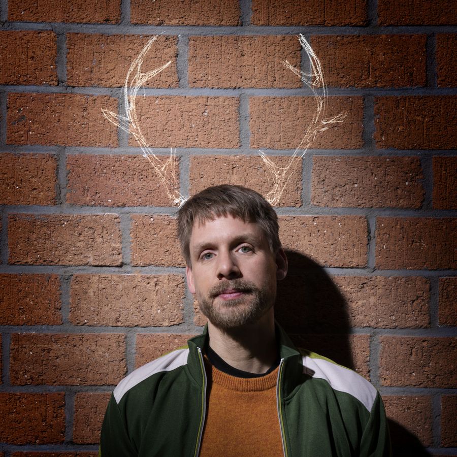 Thijs staat voor een bakstenen muur en kijkt neutraal de camera in. Boven zijn hoofd zijn rendiertakken getekend op de muur.
