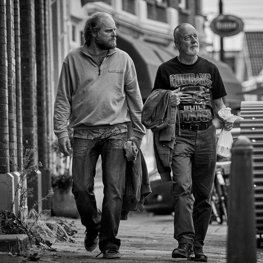 Zwart wit foto met daarop twee mannen lopend over straat. 